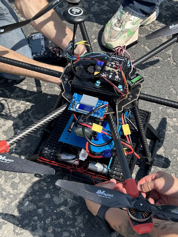 People working on the hexacopter with the ground robot mounted, outdoors on asphalt