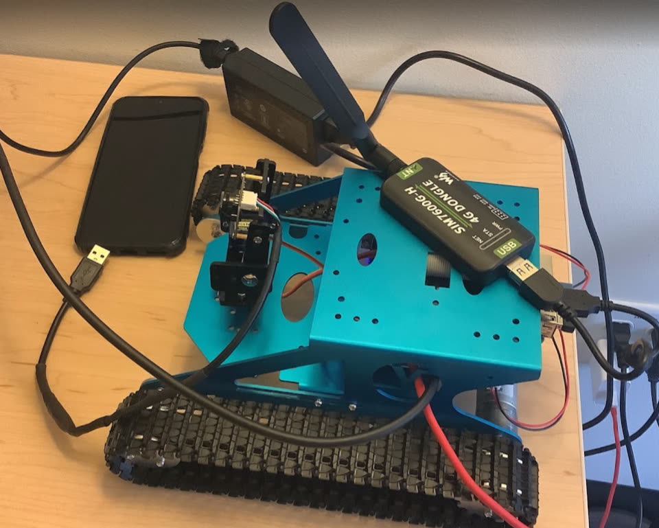 Blue tracked ground robot on a desk with cables and a phone