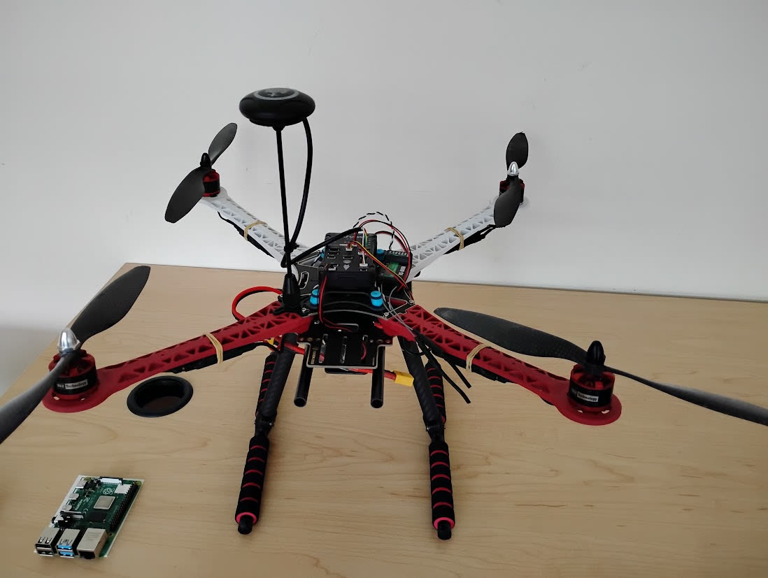 Red F450-style quadcopter on a table with a Raspberry Pi beside it